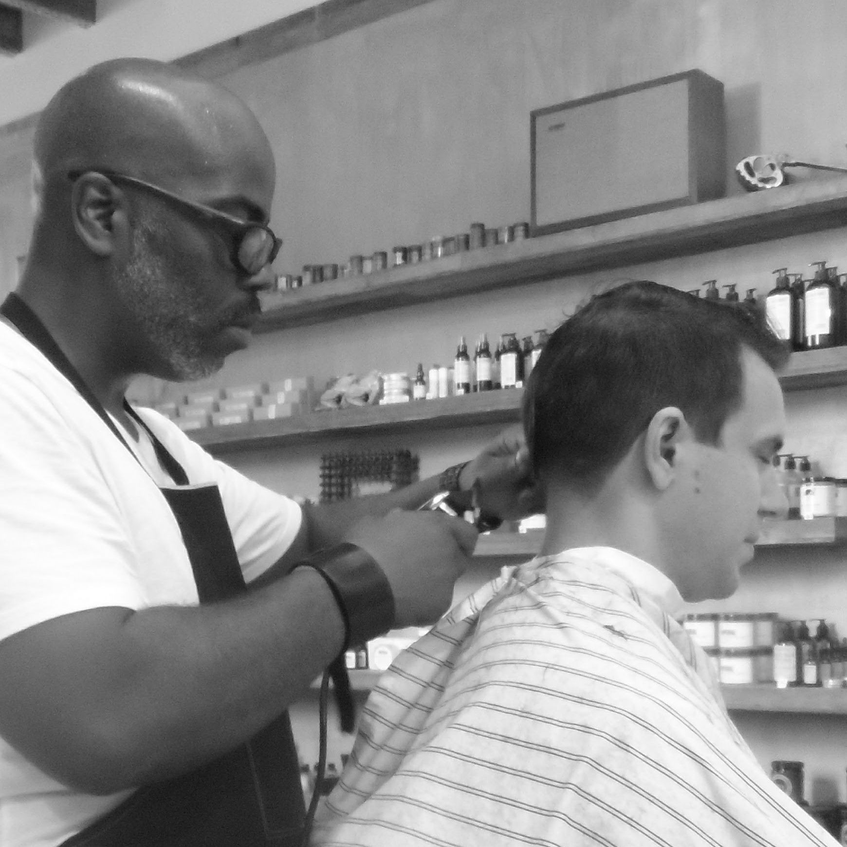 Clippers running through a client's hair with the shop shelves behind